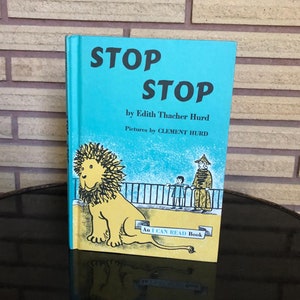 May include: A vintage children's book titled "STOP STOP" by Edith Thacher Hurd, with illustrations by Clement Hurd. The cover is turquoise with a yellow lion illustration and the text "An I CAN READ Book".