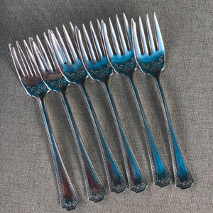 May include: Set of eight silver forks with ornate designs. The forks are arranged in a row, with the handles pointing towards the right.
