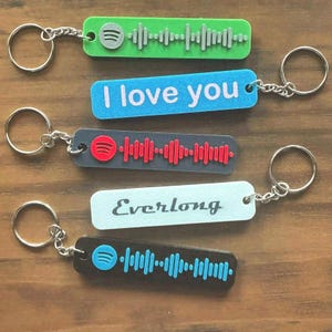 May include: Keychains in green, blue, gray, and black with silver key rings. The keychains feature Spotify codes and the text "I love you" and "Everlong". The Spotify logo is visible on some keychains.