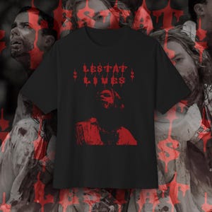 May include: Black t-shirt featuring the red text "LESTAT LIVES" and a red graphic of a person. The background has a repeating pattern of faces and red drips. A gothic-themed design.