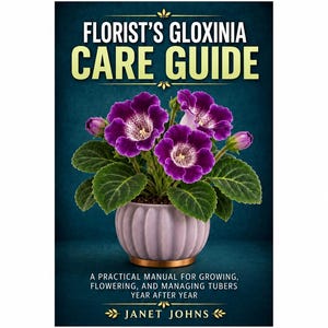 May include: A book titled Florist's Gloxinia Care Guide by Janet Johns. The cover features a potted plant with vibrant purple flowers and green leaves in a ribbed lavender pot, set against a dark blue background with gold text accents.