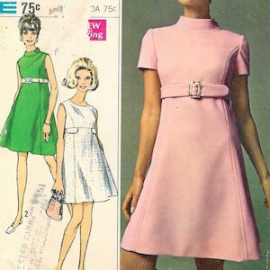 Op de afbeelding: Een Simplicity naaipatroon-envelop voor een jurk in junior maat 11 met een borstomvang van 85 cm. De hoes bevat illustraties en een foto van een jurk met korte mouwen, een hoge hals en een ceintuur in roze, groen en wit.