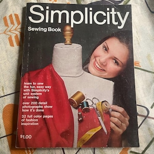 May include: A vintage Simplicity Sewing Book with a black cover featuring a dress form draped in red fabric, sewing notions, and text. The cover includes the title, instructional text, and a price of $1.00, showcasing a guide for sewing techniques.