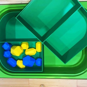 May include: A vibrant green plastic activity tray with a lid, containing blue and yellow geometric shapes. The tray is divided into sections, with the lid partially open. The shapes are various sizes and are designed for play and learning.