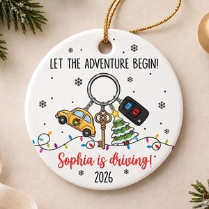 May include: A round white ceramic ornament with a gold string. It features the text LET THE ADVENTURE BEGIN!, a keychain with a yellow car, a key, a Christmas tree, and a car fob. Below is the text Sophia is driving! and 2026.