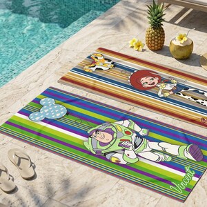 Puede incluir: Toallas de playa con los personajes de dibujos animados Buzz Lightyear y Jessie de Toy Story, y un dise&ntilde;o de Mickey Mouse. Las toallas tienen patrones de rayas coloridas y est&aacute;n cerca de una piscina.