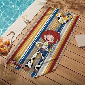 Puede incluir: Una toalla de playa colorida con una imagen de dibujos animados de Jessie de Toy Story, con un sombrero rojo y pantalones con estampado de vaca. La toalla tiene rayas verticales en rojo, amarillo, azul y blanco. El nombre "Sandra" est&aacute; impreso.