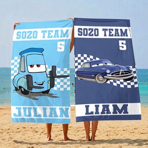 May include: Two beach towels with cartoon car designs. One is light blue with a cartoon truck and the name "JULIAN". The other is navy blue with a vintage car and the name "LIAM". Both towels have "SOZO TEAM 5" printed on them.
