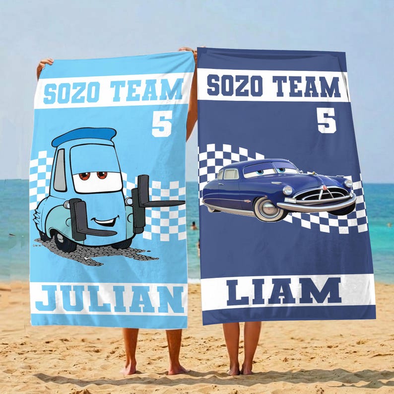May include: Two beach towels with cartoon car designs. One is light blue with a cartoon truck and the name "JULIAN". The other is navy blue with a vintage car and the name "LIAM". Both towels have "SOZO TEAM 5" printed on them.