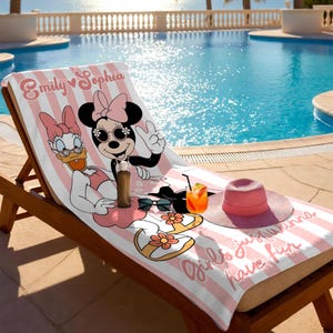 May include: A pink and white striped beach towel featuring Minnie Mouse and Daisy Duck. The towel has the text "Emily Sophia" and "Girls just wanna have fun". A pink sun hat, sunglasses, and a drink are on the towel.