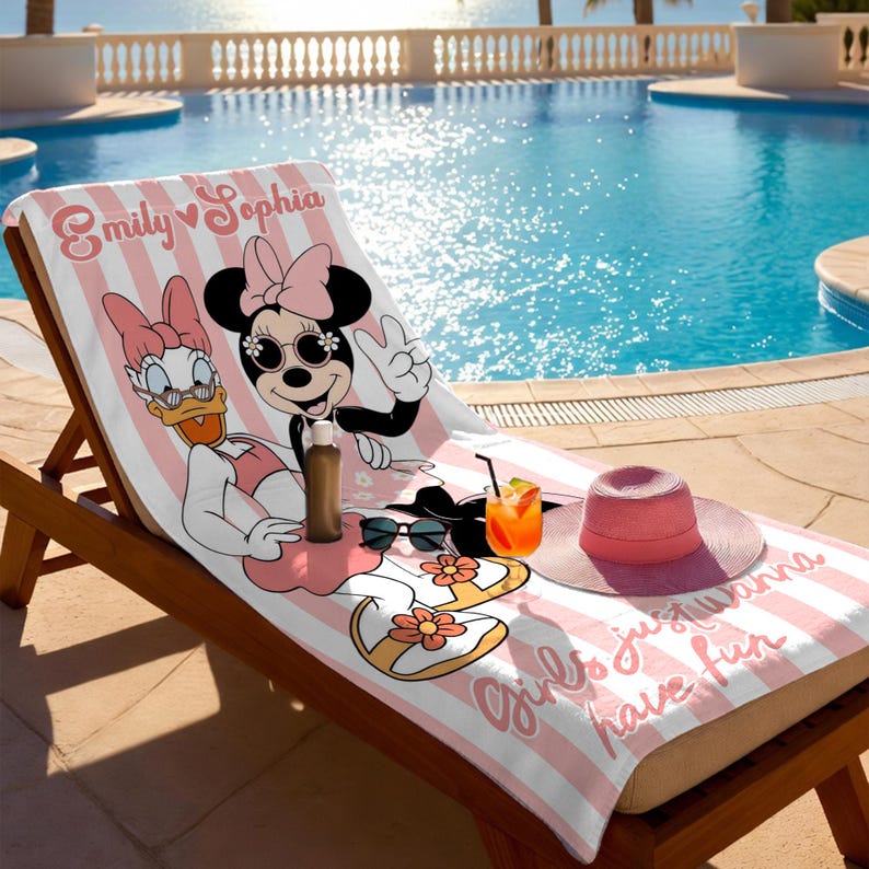 May include: A pink and white striped beach towel featuring Minnie Mouse and Daisy Duck. The towel has the text "Emily Sophia" and "Girls just wanna have fun". A pink sun hat, sunglasses, and a drink are on the towel.
