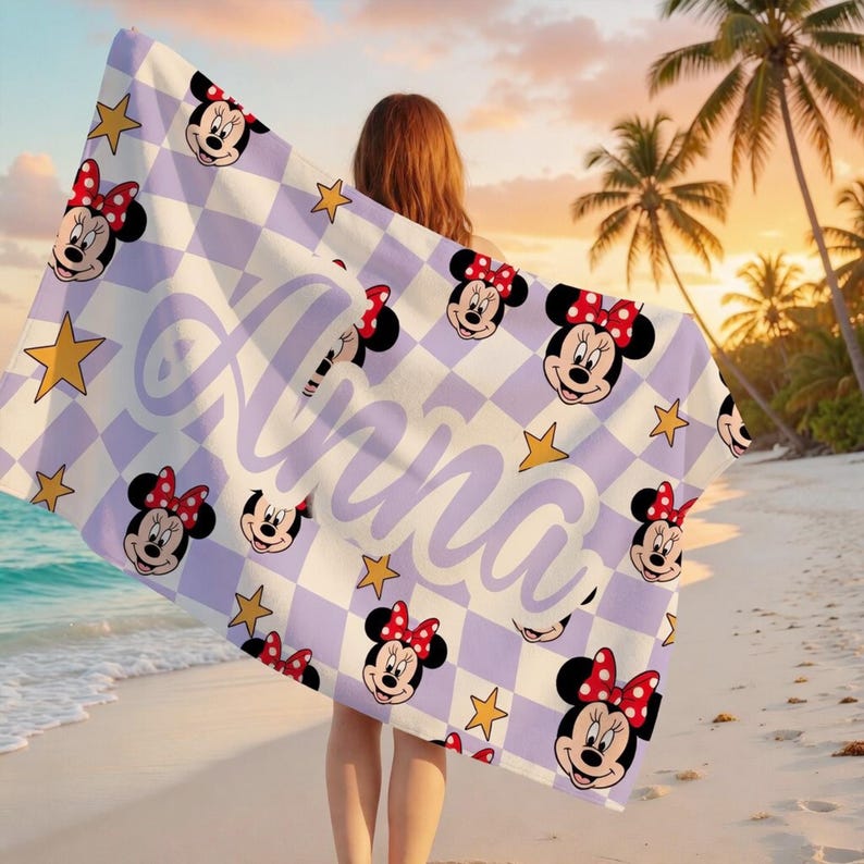 Peut inclure: Une serviette de plage avec un motif r&eacute;p&eacute;t&eacute; de visages de Minnie Mouse avec des n&oelig;uds rouges, des &eacute;toiles dor&eacute;es et le nom "Anna" en &eacute;criture lavande. La serviette a un fond &agrave; carreaux blanc et lavande.