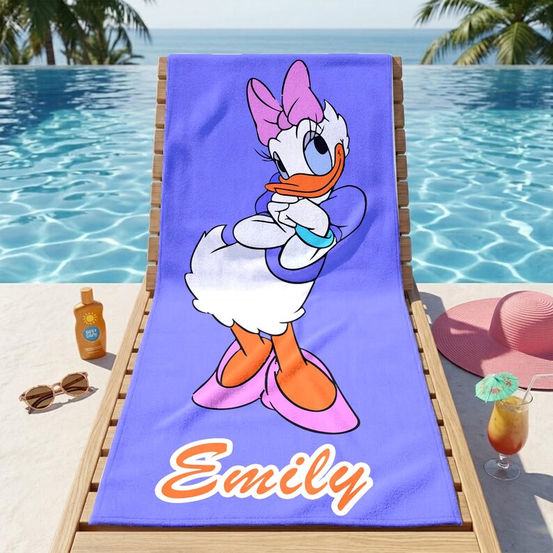 K&ouml;nnte beinhalten: Ein lila Strandtuch mit der Cartoonfigur Daisy Duck. Das Handtuch hat den Namen "Emily" in orangefarbener Schrift. Das Handtuch liegt auf einer Holzliege in der N&auml;he eines Pools, mit Sonnenbrille, Sonnencreme und einem Cocktail.