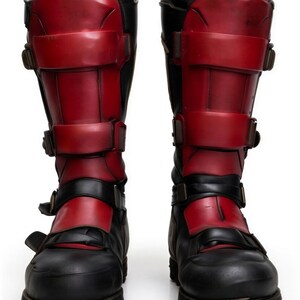 May include: A pair of black and red boots featuring multiple straps and buckles. The boots have a robust sole and are constructed from a blend of leather and synthetic materials. The upper section of the boots is red, with the lower part in black.