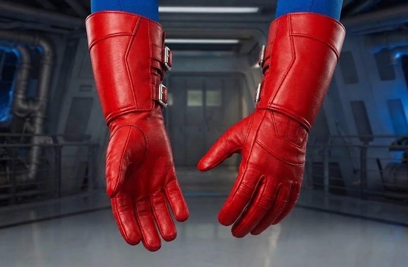 K&ouml;nnte beinhalten: Ein Paar leuchtend rote Lederhandschuhe mit langen Manschetten und silbernen Schnallen. Die Handschuhe weisen Gebrauchsspuren auf, mit sichtbaren Knitterfalten. Sie scheinen Teil eines Kost&uuml;ms oder einer Uniform zu sein. Der Hintergrund ist ein verschwommener Innenraum mit industriellen Elementen.