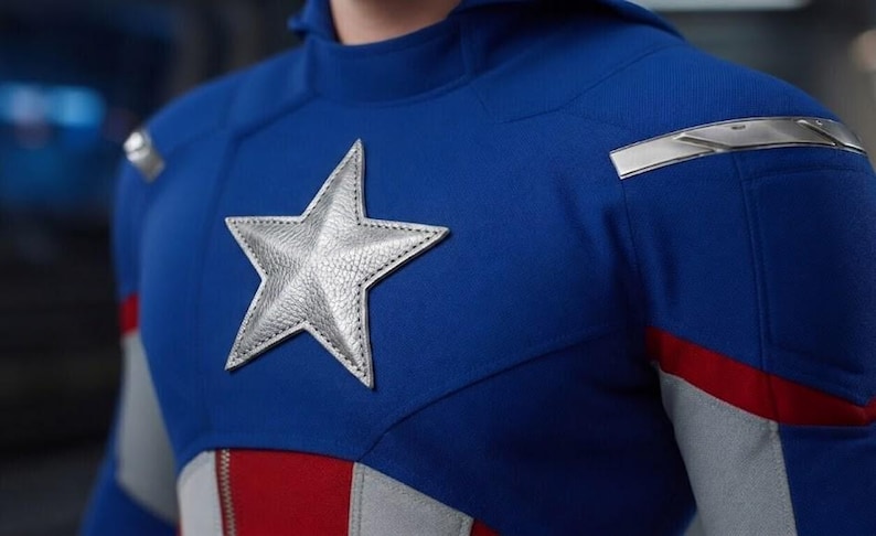 K&ouml;nnte beinhalten: Nahaufnahme eines blauen Superhelden-Kost&uuml;ms mit einem gro&szlig;en silbernen Sternemblem auf der Brust. Das Kost&uuml;m hat rote und wei&szlig;e Akzente und silberne Schulterdetails. Das Gesamtdesign ist patriotisch.
