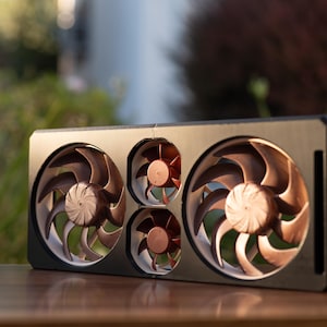 May include: A black computer component with four copper-colored fans. The fans are arranged in a rectangular pattern, with two larger fans on the top and two smaller fans below. The blades have a curved design.