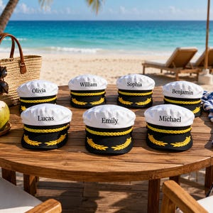 May include: Seven white captain hats with black brims and yellow braided trim featuring embroidered gold laurel leaves. Each hat is personalised with a unique name including Olivia, William, Sophia, Benjamin, Lucas, Emily, and Michael.