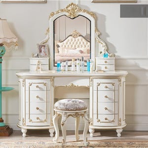 Peut inclure: Une coiffeuse blanche avec un grand miroir, des tiroirs et un tabouret assorti. La coiffeuse présente des accents dorés et des détails ornés. Le miroir est encadré d'une bordure dorée. Le tabouret a une assise à motifs floraux.