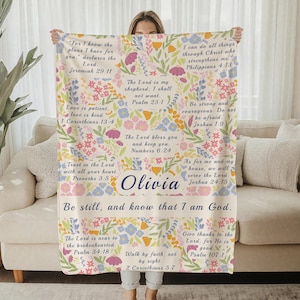 May include: A cream-colored blanket with a floral pattern in pastel colors. The blanket features inspirational quotes and the name "Olivia" in navy blue. The design includes various flowers and leaves.