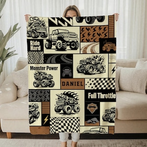 May include: A beige and black blanket with a patchwork design of monster trucks, lightning bolts, and chequered flags. The blanket has the words "Ride Hard", "Monster Power", "Daniel", and "Full Throttle" printed on it.