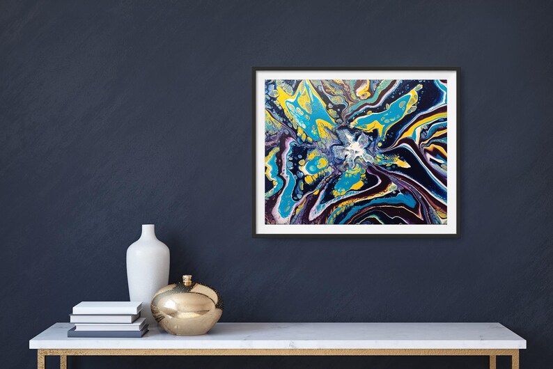 K&ouml;nnte beinhalten: Abstrakter Kunstdruck in einem schwarzen Rahmen. Das Kunstwerk zeigt ein lebendiges, farbenfrohes Design mit Blau-, Gelb- und Lilat&ouml;nen. Das Gem&auml;lde wird auf einem wei&szlig;en Tisch mit goldenem Sockel zusammen mit dekorativen Gegenst&auml;nden ausgestellt.