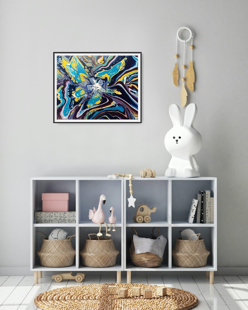 K&ouml;nnte beinhalten: Abstrakter Kunstdruck in einem schwarzen Rahmen. Das Kunstwerk zeigt eine lebendige Mischung aus Farben, darunter Gelb, T&uuml;rkis und Marineblau, die ein dynamisches und flie&szlig;endes Design erzeugt. Das Gem&auml;lde wird &uuml;ber einem wei&szlig;en Aufbewahrungsm&ouml;bel mit dekorativen Gegenst&auml;nden ausgestellt.