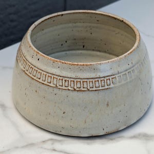 May include: A set of three ceramic mugs with a speckled, matte finish. The mugs are in shades of cream, light gray, and dark gray. Each mug has a simple, minimalist design, perfect for coffee or tea.