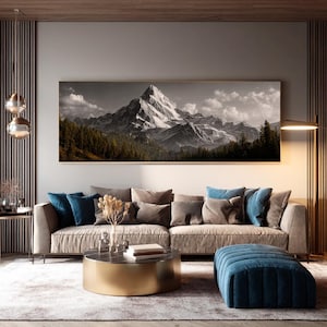 May include: A living room scene featuring a large framed black and white mountain landscape print above a beige sofa with blue and gray pillows. A gold coffee table, blue ottoman, and a floor lamp complete the modern decor.