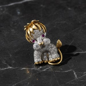 May include: A gold and silver lion brooch with ruby eyes and diamond accents. The lion's mane and tail are gold, while the body is encrusted with diamonds. The brooch is set against a dark, marble-like surface.