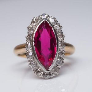 Puede incluir: Anillo de oro con una gran gema rosa brillante de forma ovalada, rodeada por un halo de gemas más pequeñas y transparentes. La banda del anillo es dorada y el engaste de la piedra rosa es plateado.