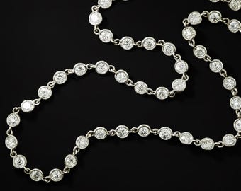 May include: A silver necklace with numerous round, clear gemstones set in individual bezels. The necklace is displayed against a black background, highlighting the sparkle of the stones. The chain is delicate, connecting each gemstone. A piece of jewelry.