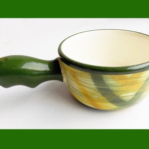 Puede incluir: Una olla de fondue de cerámica verde con un diseño a rayas amarillo y verde. La olla tiene un asa y es perfecta para servir fondue de queso o chocolate.