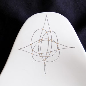May include: White ceramic serving dish with a black and gold geometric design. The design features a series of overlapping circles and lines.