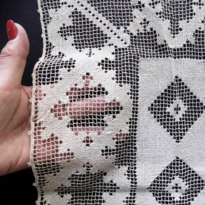May include: Close-up of a white crocheted lace fabric with a geometric pattern. The fabric has a delicate, intricate design with small holes and a grid-like structure.