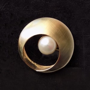 May include: A pair of gold earrings with a circular design and a white pearl in the center of each earring.