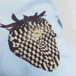 Puede incluir: Una camiseta azul claro con un dise&ntilde;o a cuadros en blanco y negro de un coraz&oacute;n con cuernos.