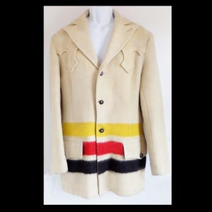 Puede incluir: Una chaqueta de lana de color crema con cuello de estilo western y un patrón de rayas de colores en la parte inferior. Las rayas son amarillas, rojas, negras y blancas.