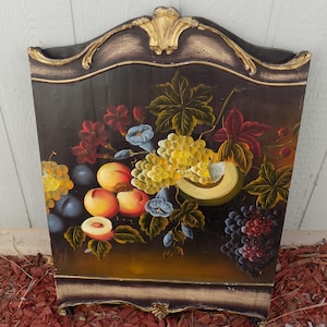 May include: A decorative wooden panel featuring a still life painting of fruit. The artwork includes grapes, peaches, and plums in vibrant colors against a dark background. The panel has a gold-colored ornate trim.
