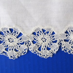 Może przedstawiać: Biały materiał bawełniany z delikatną koronkową lamówką. Koronka ma falisty wzór z motywem kwiatowym.