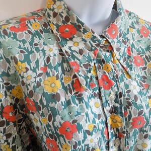 Puede incluir: Una camisa de botones con cuello de color verde, blanco y naranja con estampado floral.