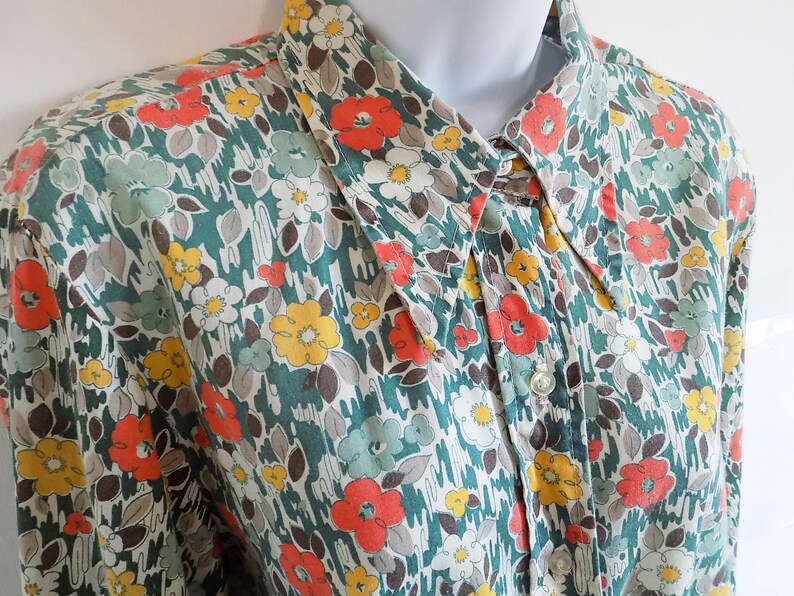 Puede incluir: Una camisa de botones con cuello de color verde, blanco y naranja con estampado floral.