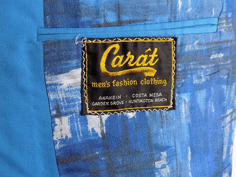 May include: A blue blazer with a black label that reads "Carat men's fashion clothing" with the locations "Anaheim, Costa Mesa, Garden Grove, Huntington Beach" printed below.