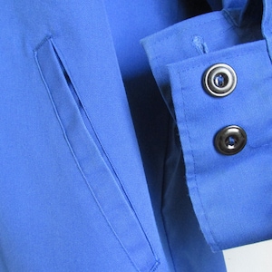 Puede incluir: Primer plano de una camisa azul con un bolsillo y dos botones negros en el pu&ntilde;o.