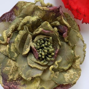 May include: A large, green and brown fabric flower with a textured, almost mossy, appearance. The flower has a center made of small, green beads.
