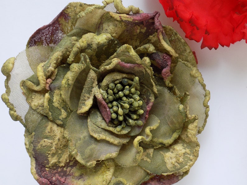 May include: A large, green and brown fabric flower with a textured, almost mossy, appearance. The flower has a center made of small, green beads.