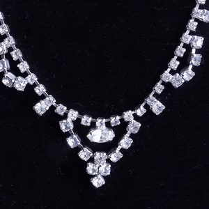 May include: A silver necklace with a teardrop-shaped pendant made of clear rhinestones.