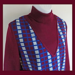 May include: A burgundy turtleneck sweater with a geometric pattern of blue and white squares. The sweater has a V-neck opening.