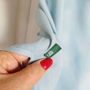 Puede incluir: Una camisa azul claro con una etiqueta verde que tiene una flor blanca.