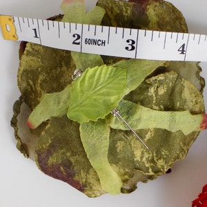 May include: A green and brown fabric rose with a green leaf and a silver pin. The rose is about 2 inches in diameter.